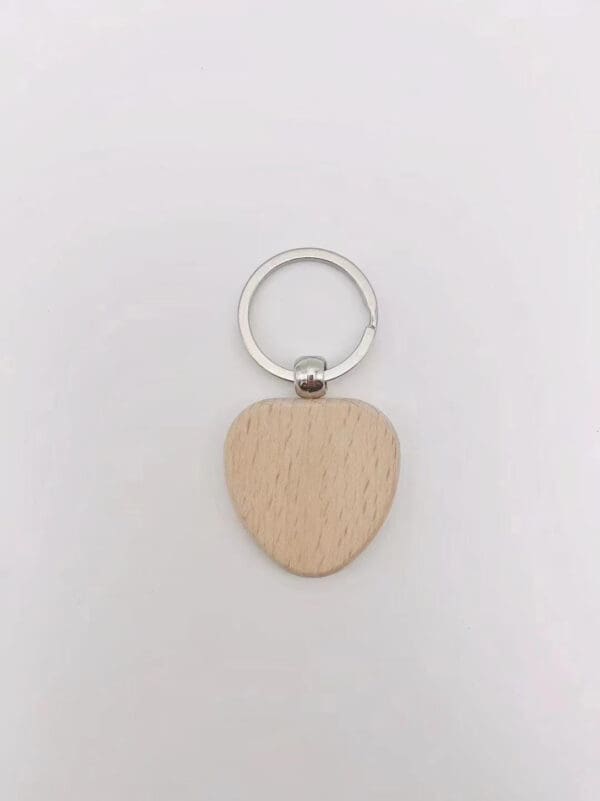 A metal keyring with a flat, smooth, light-colored wooden heart-shaped pendant attached—this charming wooden keychain rests on a plain white background.