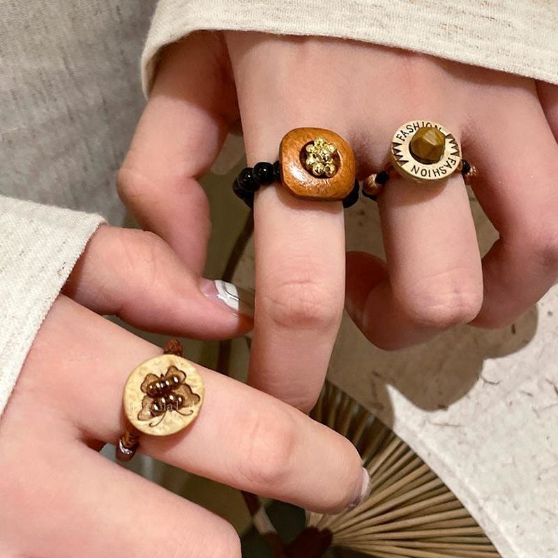 A close-up of hands wearing three eco-friendly wooden rings with different designs, including bees and engraved text, on the index and middle fingers.