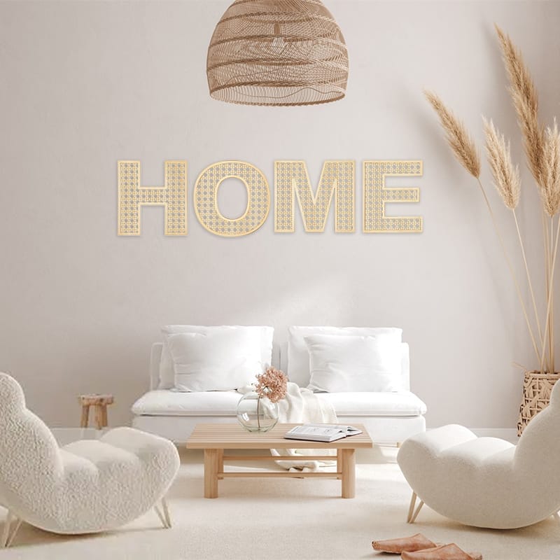 A minimalist living room with white furniture, a wooden coffee table, pampas grass, and large "HOME" letters on the wall.