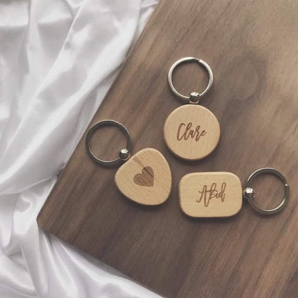 Three wooden keychains on a wooden surface: one with the name "Clare," one with a heart symbol, and one with the name "Afad.