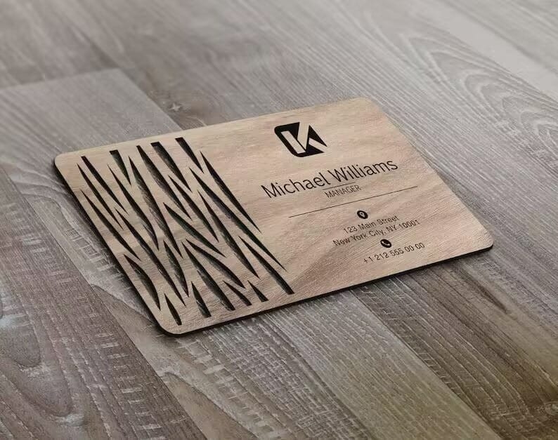 Wooden Business Card with engraved abstract lines, company logo, and contact details for Michael Williams, a marketer. This Laser Cut Personalized Wood Card is displayed on a wood surface.