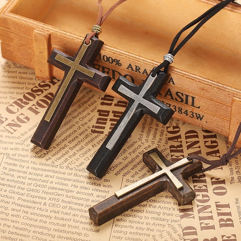 Three wooden cross necklaces with black cords are displayed on newspaper, a wooden box in the background adding charm. This vintage necklace style doubles as a unisex sweater chain, perfect for casual or classic looks.