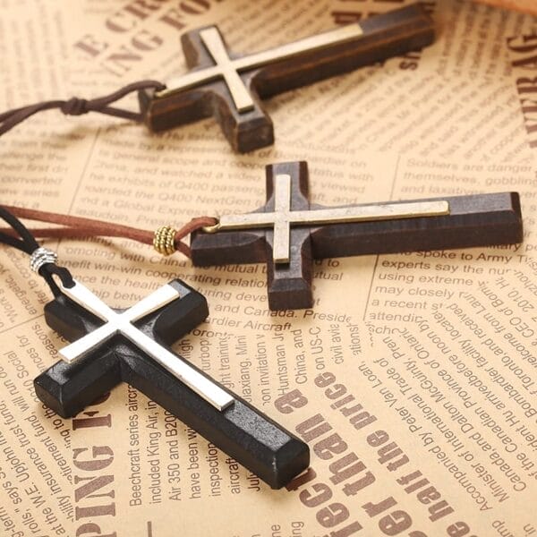 Three Wooden Cross Necklaces with metal inlays rest on sheets of printed newspaper, offering a timeless vintage necklace style perfect as a unisex sweater chain.