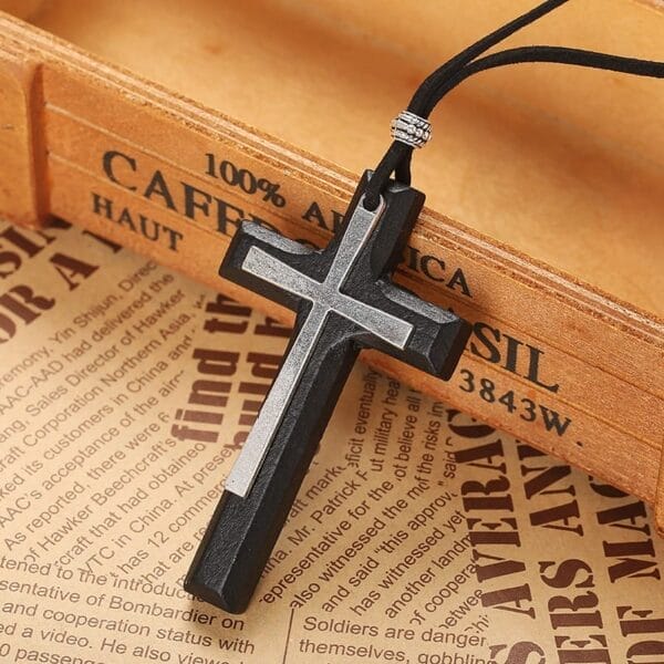 A Vintage Wooden Cross Necklace with black and silver details rests on a wooden box, with newspaper pages underneath—a timeless unisex sweater chain perfect for any style.