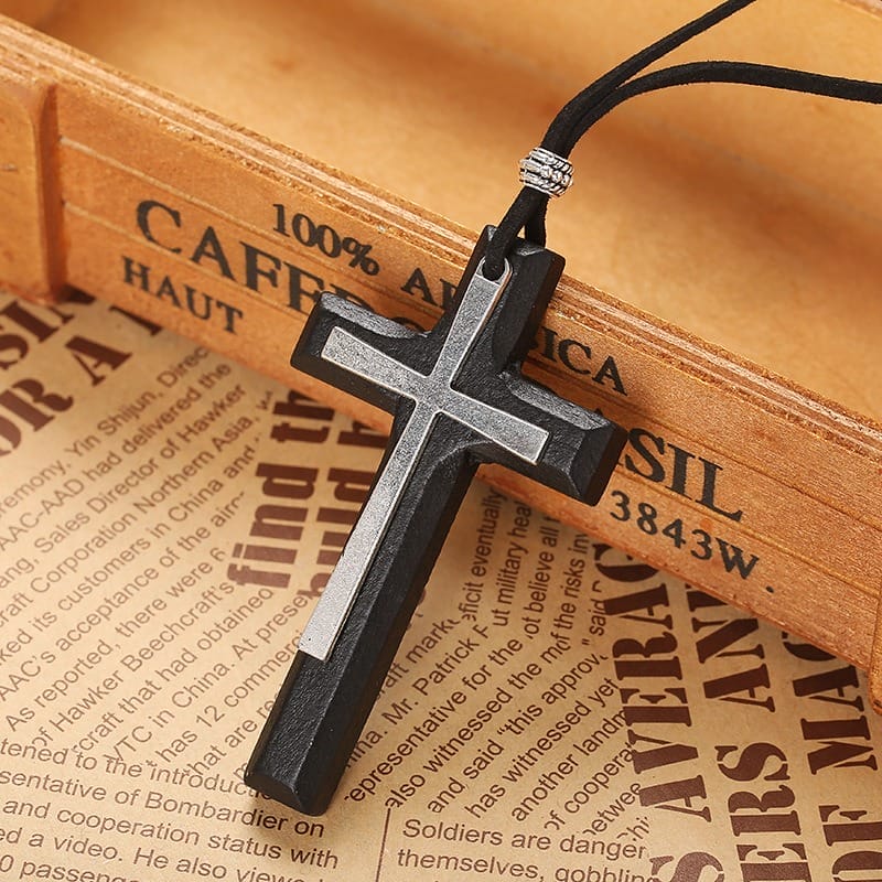 A Vintage Wooden Cross Necklace with black and silver details rests on a wooden box, with newspaper pages underneath—a timeless unisex sweater chain perfect for any style.