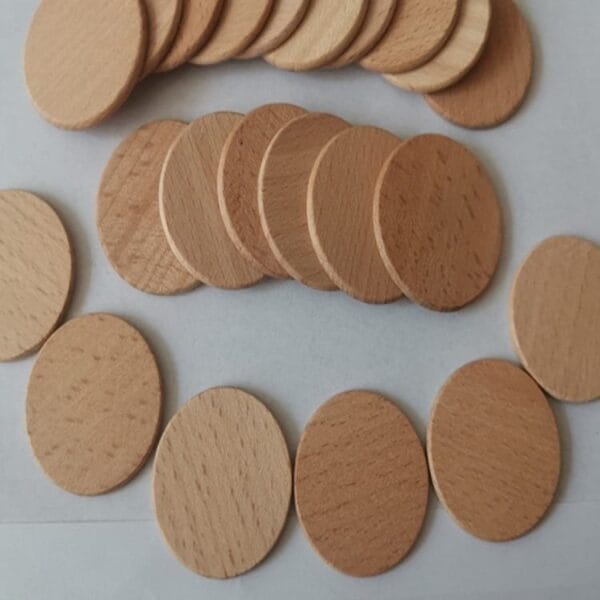 Several round, flat, light brown wooden tokens made of beech wood are arranged in three rows on a white surface.