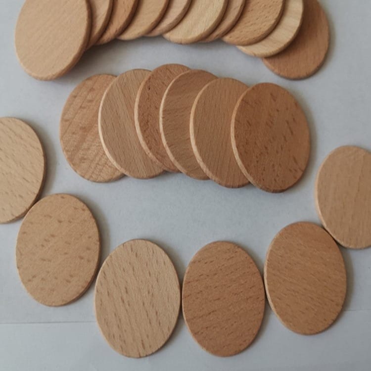 Several round, flat, light brown wooden tokens made of beech wood are arranged in three rows on a white surface.