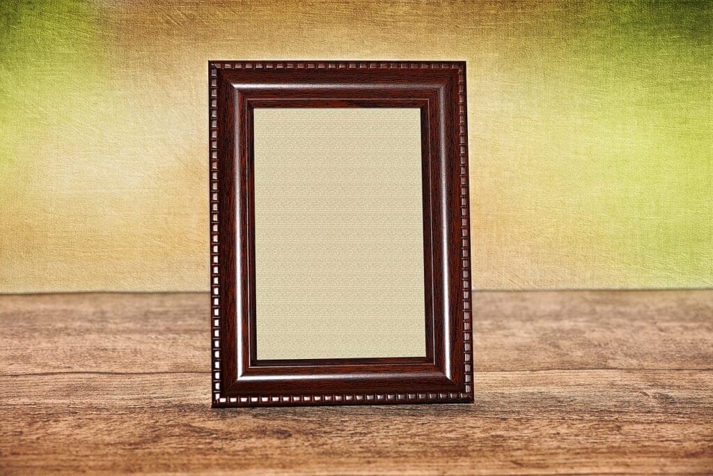 A blank picture frame with a dark brown, ornate border stands upright on a wooden surface against a textured, gradient background—perfect inspiration for DIY enthusiasts or those seeking unique wood cutout ideas for Father's Day.