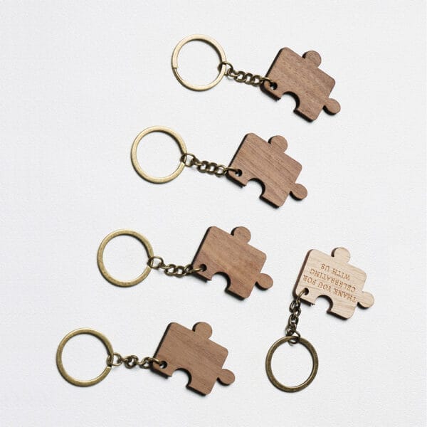 Personalized Wooden Keychains Five brass keychains with wooden keychains piece-shaped charms are arranged on a white surface; one charm reveals engraved text on its back.