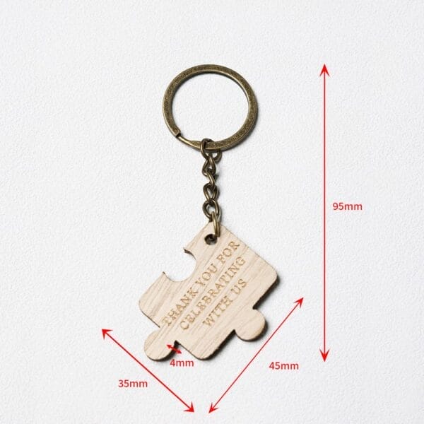 A keychain with a wooden puzzle piece engraved "THANK YOU FOR CELEBRATING WITH US," with red arrows indicating measurements: 95mm total length, 45mm by 35mm puzzle piece.