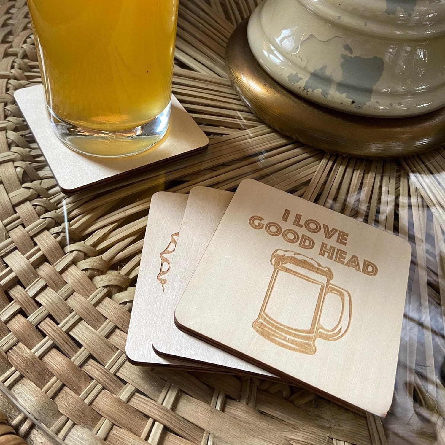 A glass of beer sits on a square wooden coaster. Nearby are three other Wooden Beer Coasters, one engraved with a beer mug and the phrase "I LOVE GOOD HEAD.