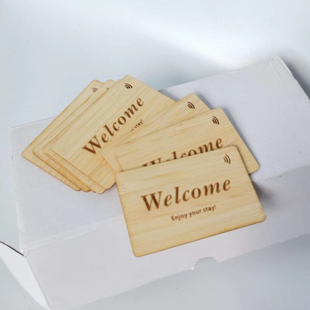 A stack of wooden key cards with "Welcome Enjoy your stay!" printed on them, placed on top of a white box.