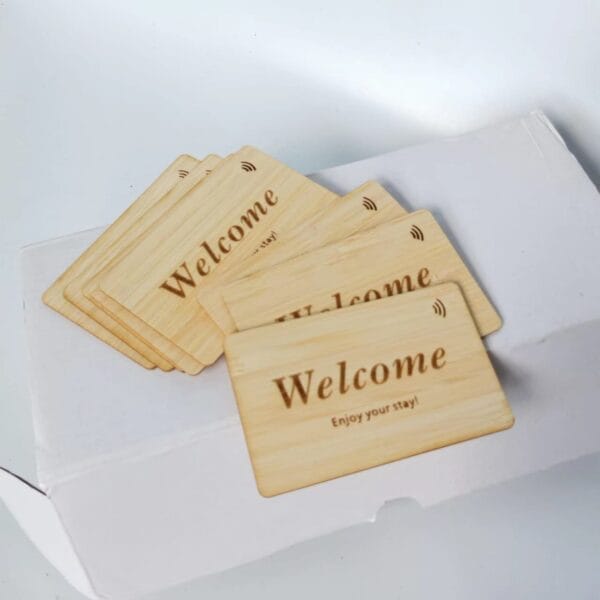 A stack of wooden key cards with "Welcome Enjoy your stay!" printed on them, placed on top of a white box.