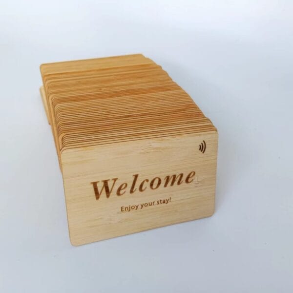 A stack of wooden cards with the text "Welcome" and "Enjoy your stay!" engraved on them, featuring a contactless symbol in the top right corner.