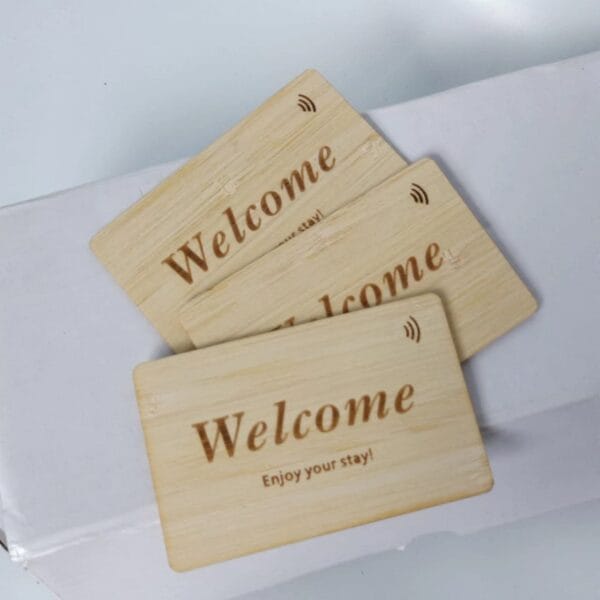 Three wooden key cards with the word "Welcome" and the phrase "Enjoy your stay!" placed on a white box.
