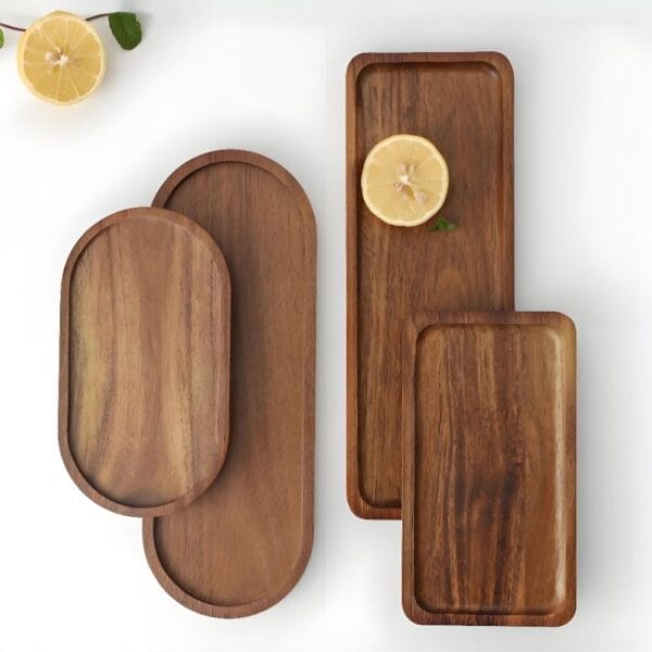 Four wooden trays of different shapes and sizes are arranged on a white surface, with two lemon halves and a mint leaf accenting each wooden tray.