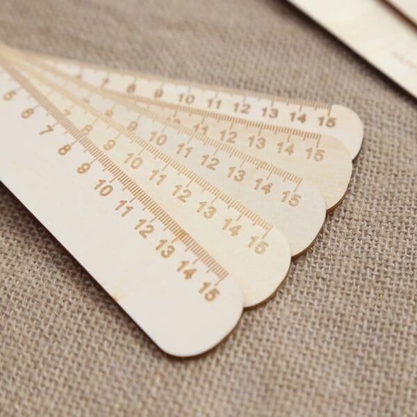 Five wooden engraved rulers with rounded ends are fanned out on a textured fabric surface, showing measurements from 0 to 15 centimeters—perfect as Laser Cut Wood Bookmarks or unique custom gifts.