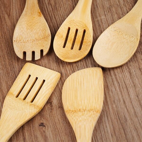 Five wooden spoons from a bamboo utensil set, each with unique shapes and slots, are neatly arranged on a wooden surface—the perfect non-stick utensils for any kitchen.