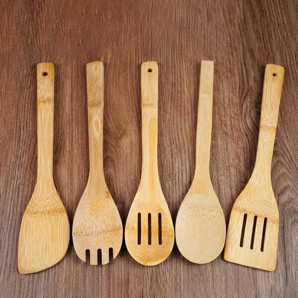 Five Wooden Spoons and spatulas, part of a Bamboo Utensil Set, are arranged side by side on a wooden surface—perfect Non-Stick Kitchen Utensils for everyday cooking.
