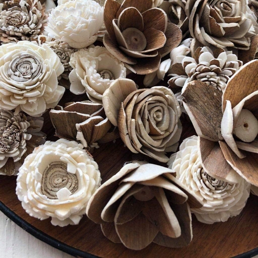 A variety of intricately carved Sola wood flowers in natural brown and cream colors are arranged closely together on a round wooden surface, making them perfect for unique wooden flower bouquets at weddings.
