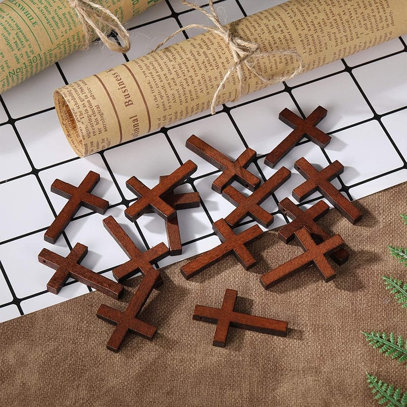 Several small wooden crosses are scattered on a brown surface, next to a rolled piece of twine-tied paper on a white grid background.