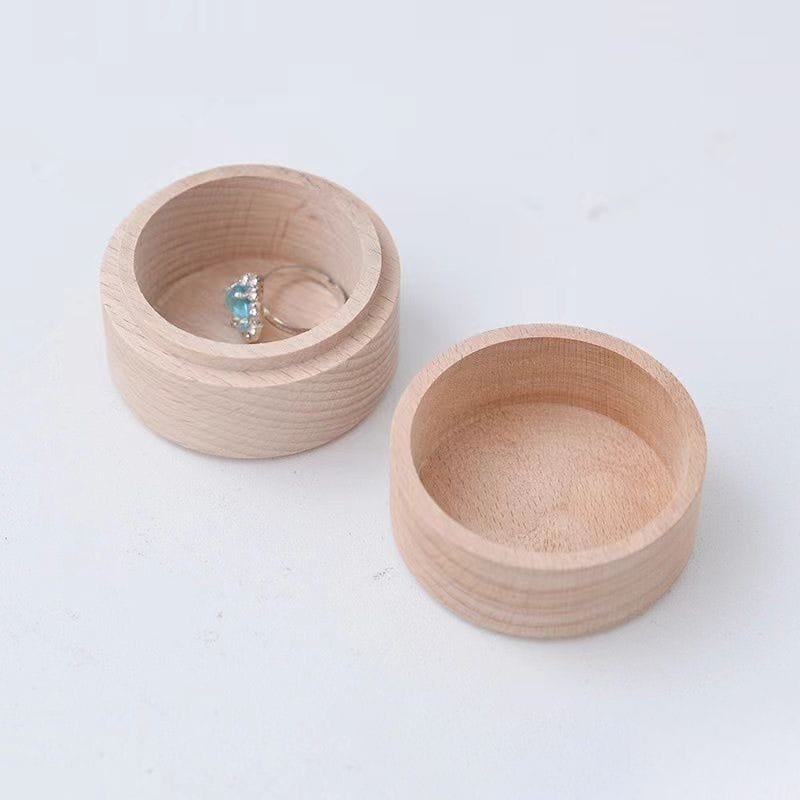 Two round, light wood containers, one with a lid removed to reveal a silver ring with a blue gemstone inside.