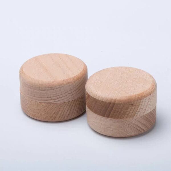 Two round, light-colored wooden containers with matching lids are placed side by side on a plain white surface.