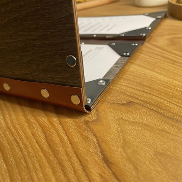 Close-up of a brown wooden menu cover with a leatherette edge, showcasing its foldable design. Wholesale restaurant menu.