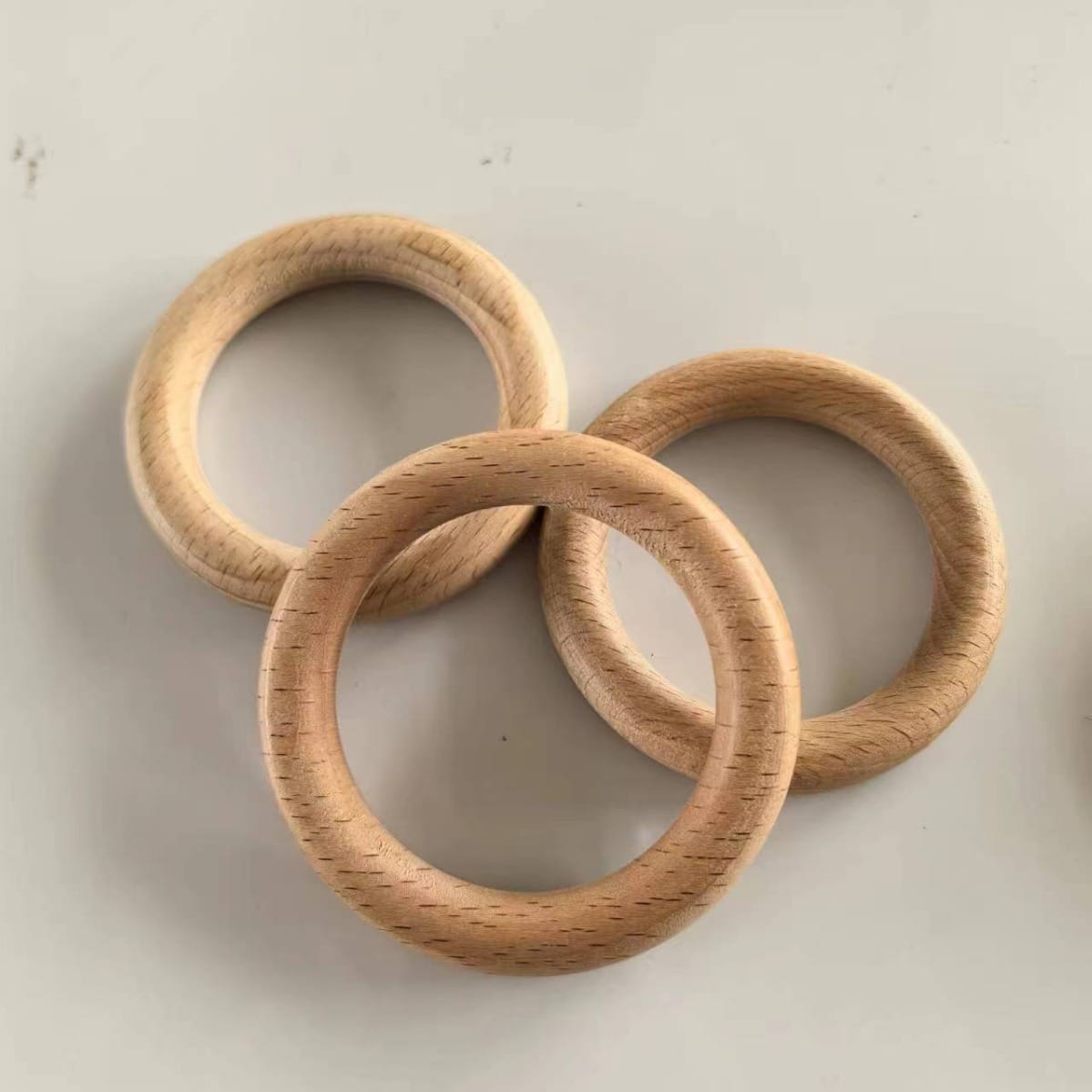 Three smooth, light beech wood rings overlap each other on a plain white surface, perfect for DIY projects or wooden ring craft supplies.