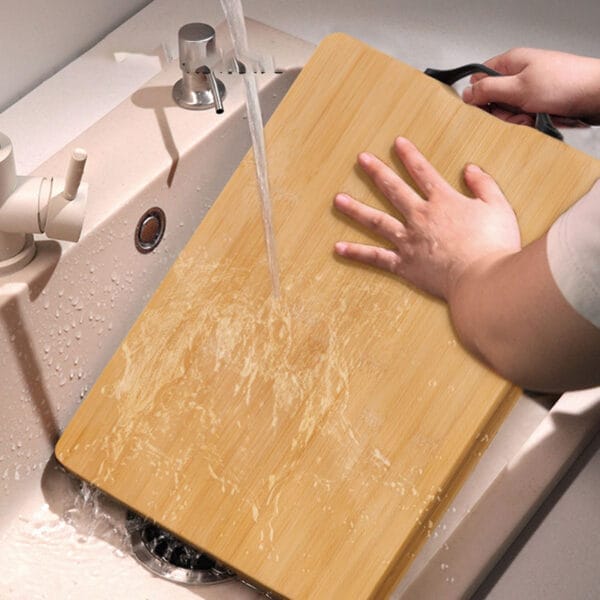 Person rinsing a large, eco-friendly bamboo cutting board under running water. Wholesale bamboo cutting boards available.