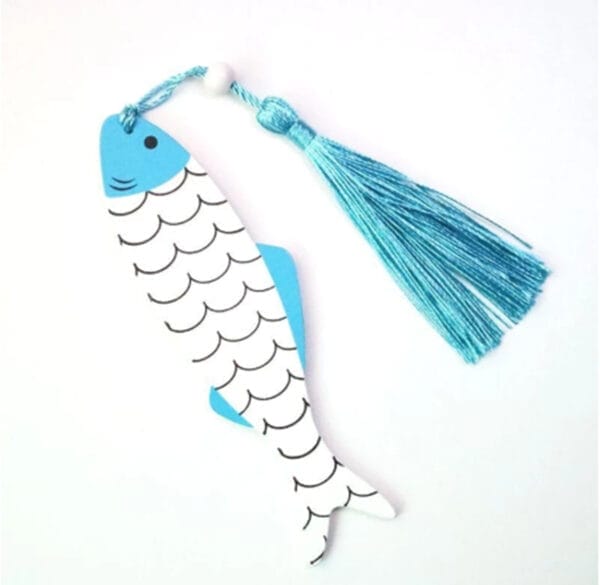 A fish-shaped wooden ornament with a blue tail, white body with black scales, and an attached blue tassel—perfect as an eco-friendly bookmark or a unique addition to your DIY wooden crafts collection—lying on a white surface.