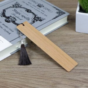 Engravable bookmarks with dark tassel, resting on a book. Customizable, standard size.