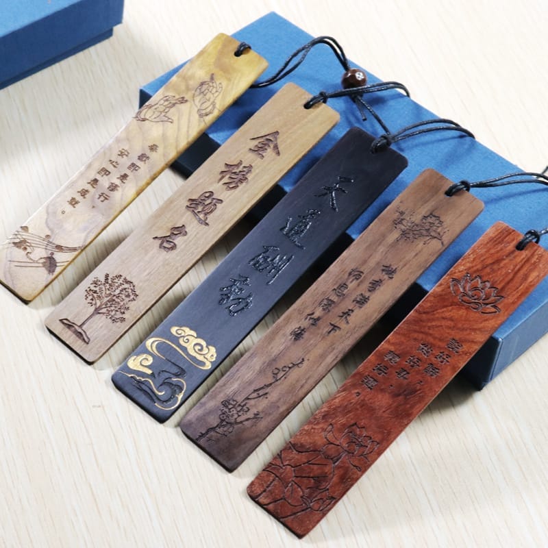Five engraved bookmarks made of wood, each featuring Chinese characters and intricate designs, with string loops for hanging, displayed on a light wooden surface.