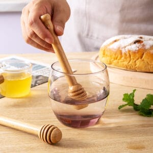 Wooden honey dippers in a glass of water. Wholesale honey dipper supplier.