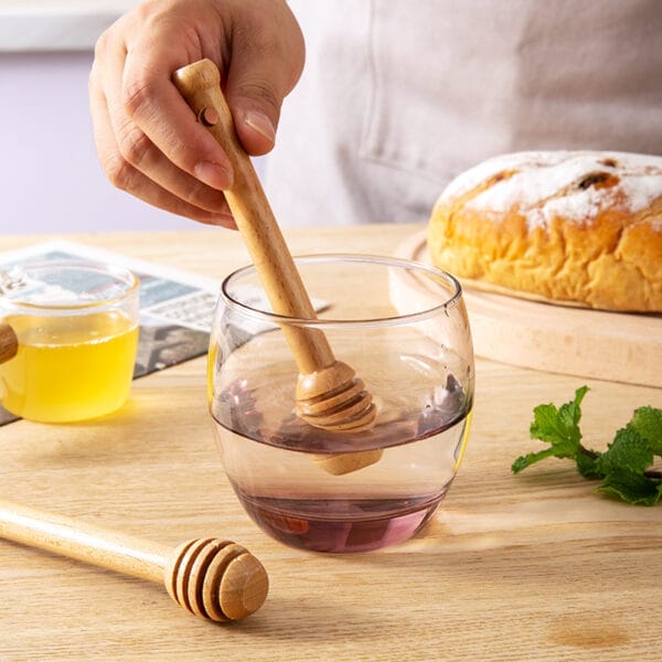 Wooden honey dippers in a glass of water. Wholesale honey dipper supplier.