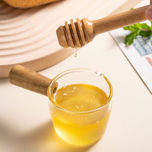 Wooden honey dipper dripping honey into a glass dish. Wholesale honey dippers available.