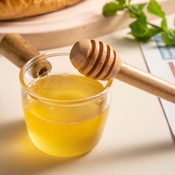 Wooden honey dipper in glass of honey. Wholesale honey dippers available.