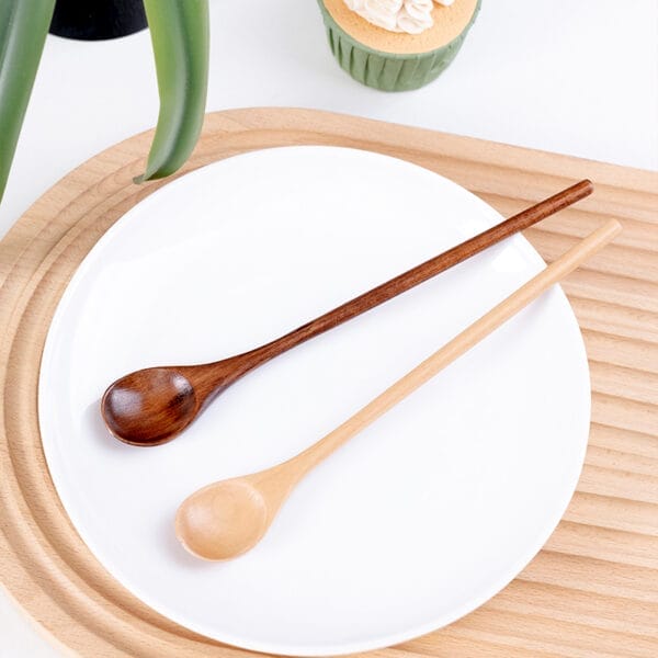 Two wooden spoons, one dark and one light, rest on a white plate. Wholesale honey spoons from a wooden spoon manufacturer.