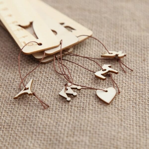 Wooden laser cut wood bookmarks with ruler edges and charming decorative charms—bird, airplane, crown, heart, and animal—make unique gifts, displayed on a burlap fabric background.