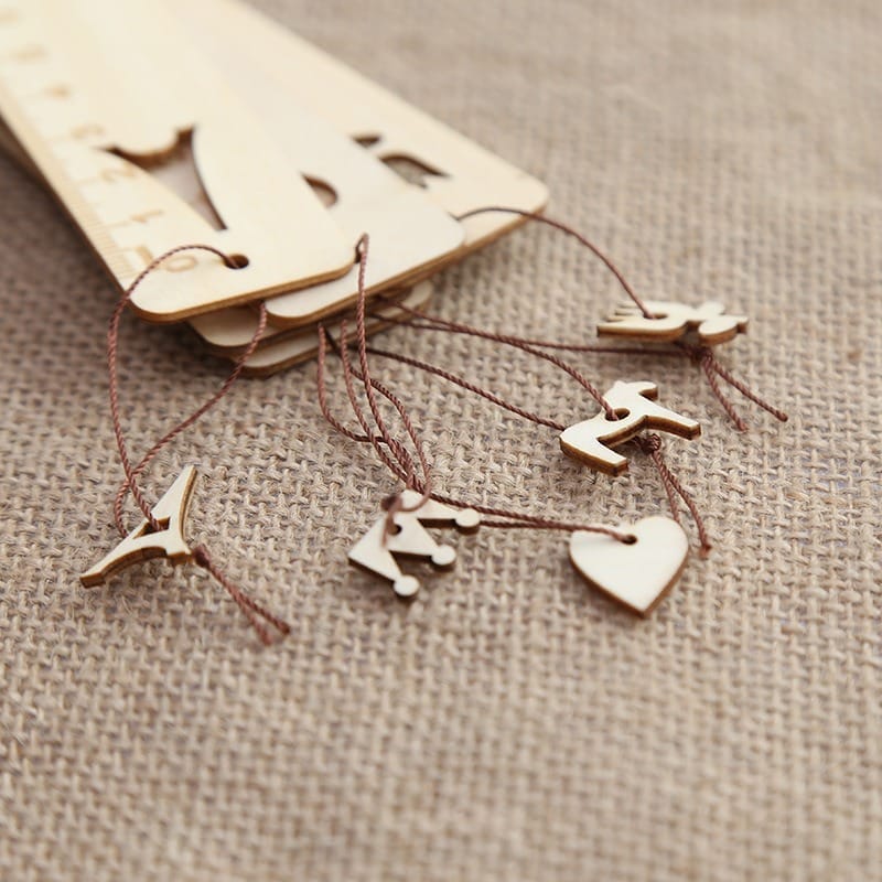 Wooden laser cut wood bookmarks with ruler edges and charming decorative charms—bird, airplane, crown, heart, and animal—make unique gifts, displayed on a burlap fabric background.