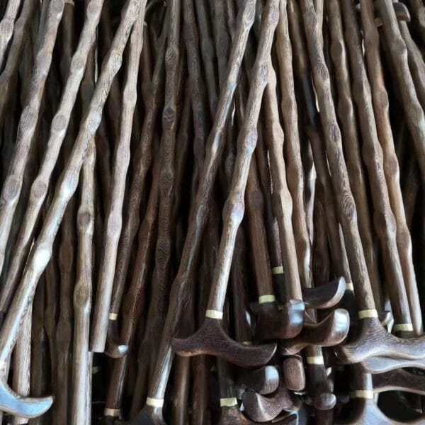 A large pile of wooden walking canes with curved handles, including elegant Red Sandalwood Canes, stacked together by a trusted wholesale supplier.