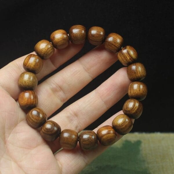 A hand holds a circular men’s wood bracelet, its uniformly sized, polished brown beads gleaming against a dark background—a stylish accessory for those seeking wholesale elegance.