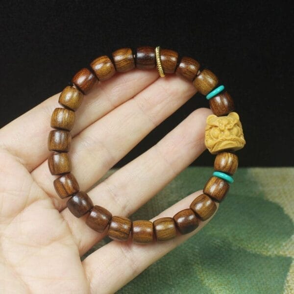 A hand holds a men's bracelet crafted with dark wooden beads, two turquoise accents, a gold bead, and a carved yellow charm—an elegant addition to wood bracelets and running style wristbands collections.