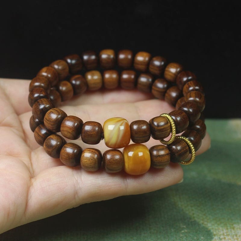 A hand holding two men’s wood bracelets, each featuring a single larger yellow bead and decorative gold rings, perfect for those seeking unique running style wristbands.