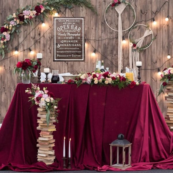 Rustic wedding reception table with custom wood open bar sign, floral arrangements, and books. "Proceed with Caution!