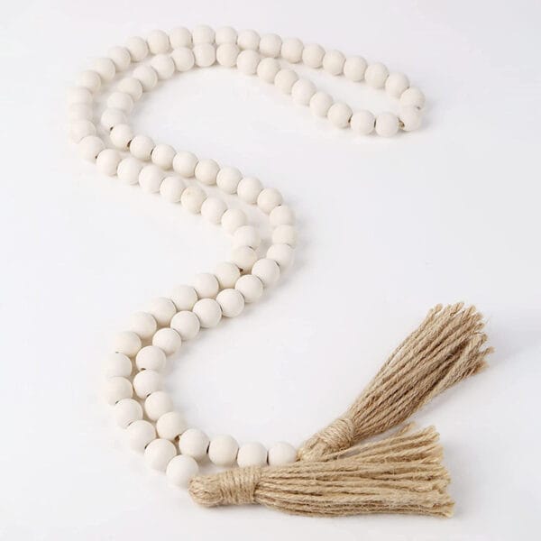 A string of matte white wood beads with two jute tassels on each end, arranged in an S shape on a white surface, makes a charming tassel string accent.