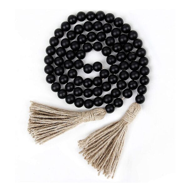 A strand of black wood beads with two beige tassels at each end, arranged in a spiral on a white background, perfect for stylish home decor.