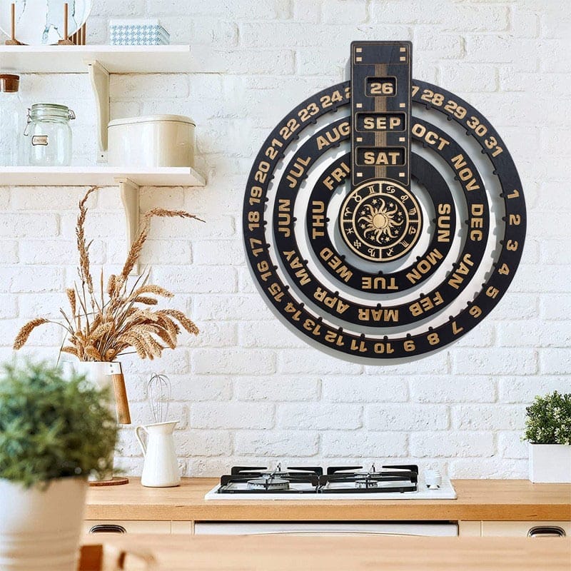 A wall-mounted wood calendar is displayed above a kitchen stove, with dried plants and kitchen items on nearby shelves against a white brick wall.