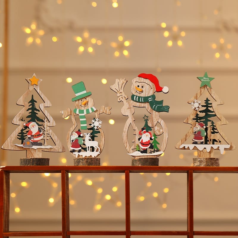 Four wood Christmas decorations featuring trees, snowmen, and Santa Claus are displayed on a ledge with warm string lights glowing softly in the blurred background.