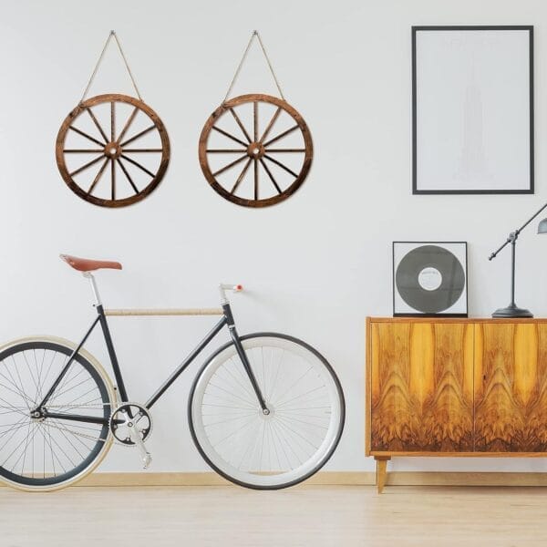 A modern room with a bicycle, a wooden sideboard, a lamp, framed art, and Rustic Wheel Decor hanging as striking accents on the white wall.